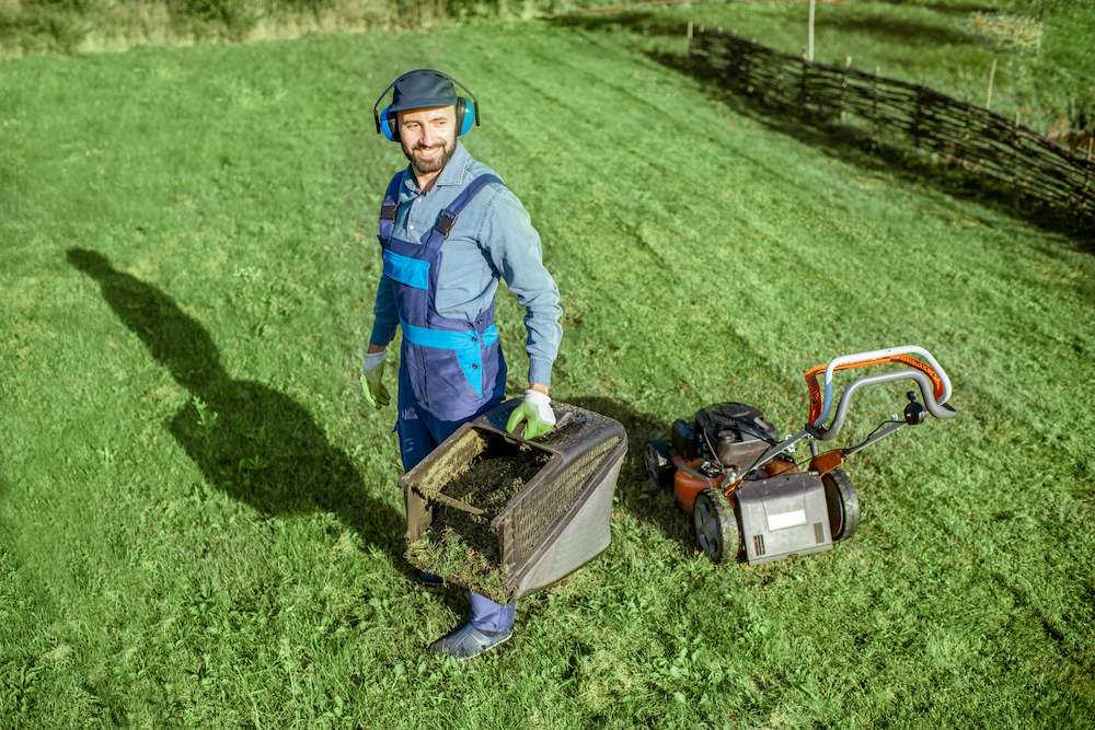 A lawn business owner empties a bag of grass while mowing a yard.